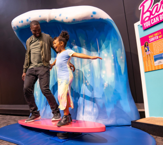 A girl and her dad experience a tidal wave exhibit in Barbie You Can Be Anything at Science Museum Oklahoma