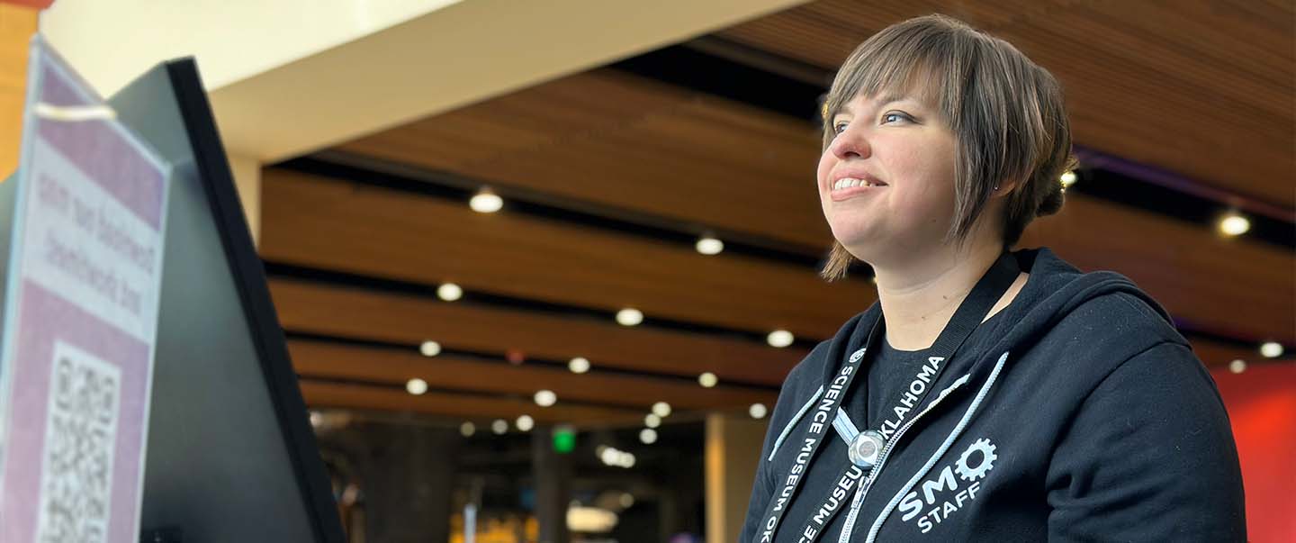 A smiling staff member welcomes guests at the front desk of Science Museum Oklahoma, ready to assist with admissions, membership, and visitor information.