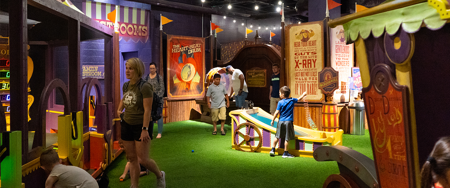 Families explore the vibrant CurioCity exhibit at Science Museum Oklahoma, filled with interactive carnival-themed health and science activities.