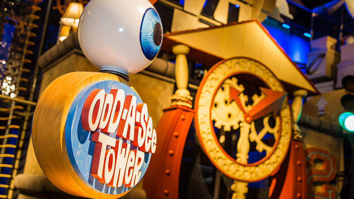 Colorful Odd-A-See Tower exhibit sign with giant eyeball and whimsical gear clock inside CurioCity at Science Museum Oklahoma.