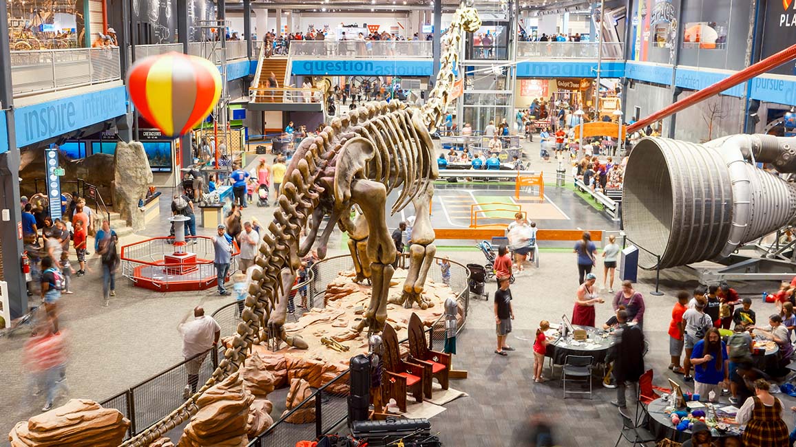 Families explore Science Museum Oklahoma’s main exhibit hall filled with hands-on STEM activities, a towering dinosaur skeleton, a hot air balloon, and a rocket engine at DiscoverFest.