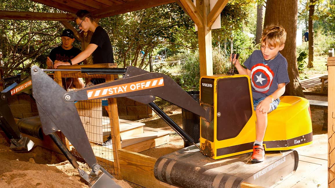 A young boy operates a kid-friendly excavator in the outdoor play area at Science Museum Oklahoma, exploring engineering and construction through hands-on STEM play. at DiscoverFest.