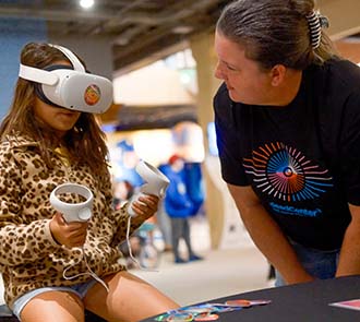A child explores virtual reality at Science Museum Oklahoma DiscoverFest while a museum educator provides guidance during an interactive, technology-focused STEM experience.