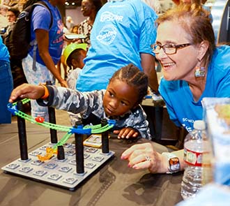 A young child engages with a hands-on STEM activity at Science Museum Oklahoma while a smiling educator encourages creativity and problem-solving during a science event.