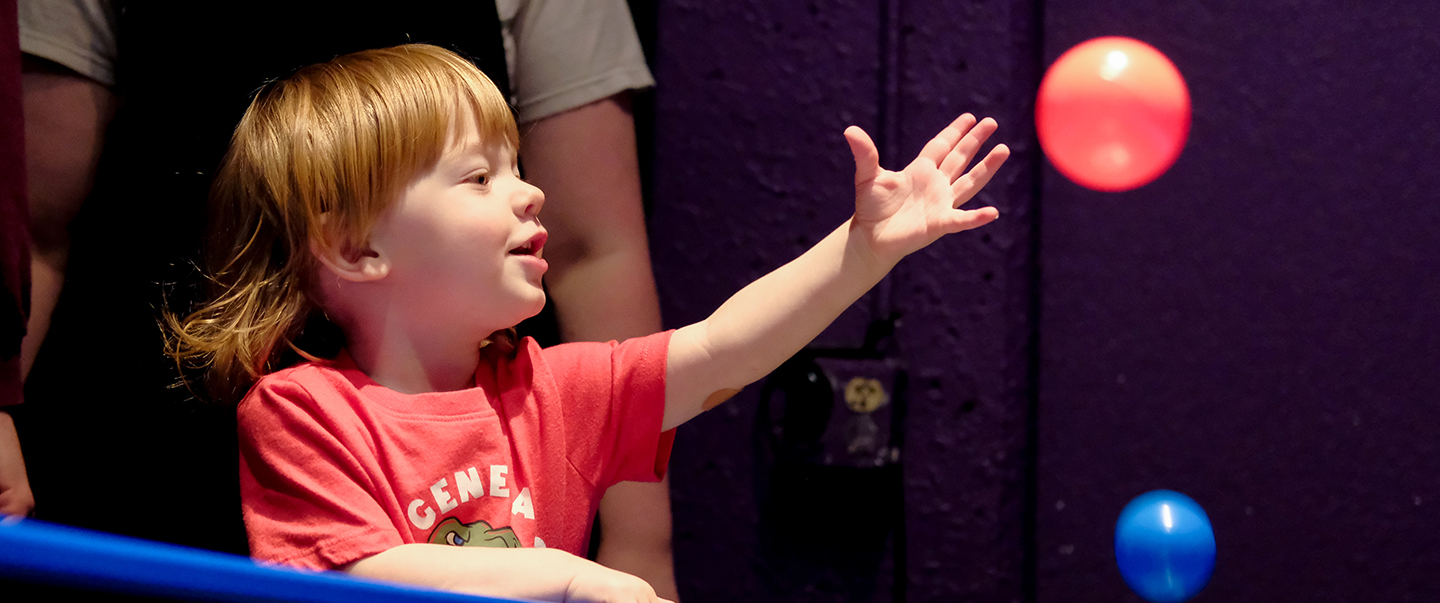 Child participates in an interactive bubble experiment at Science Museum Oklahoma, surrounded by colorful exhibits in a hands-on science gallery.