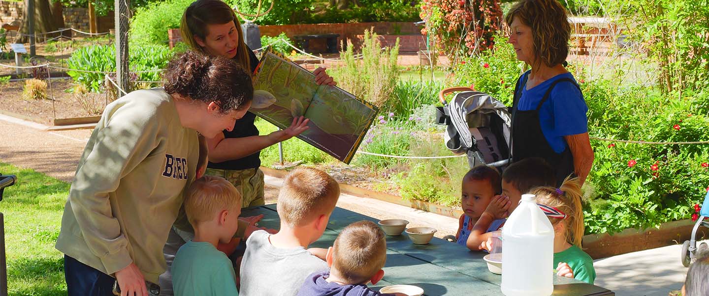 A group of young kids and toddlers listen to a story in the Gardens at Science Museum Oklahoma.