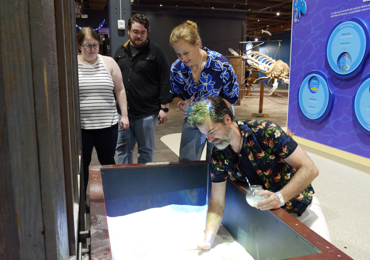 one man playing in sand at a smo21+ event while another man and two women watch with smiles