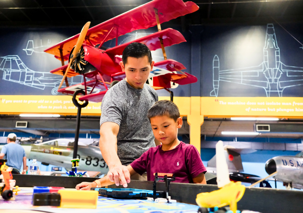 Father and son playing with robotics with large red plane in the background