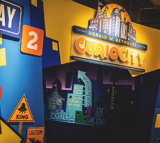 Colorful entry sign for CurioCity at Science Museum Oklahoma, an interactive cityscape exhibit designed for hands-on STEM learning and play.