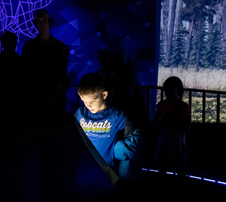A child explores a glowing interactive screen inside the immersive digital environment of Elemental Worlds at Science Museum Oklahoma.