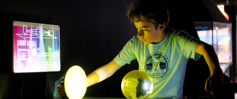 A young boy experiments with light and lenses at Science Museum Oklahoma’s hands-on optics exhibit, learning how light bends and focuses.