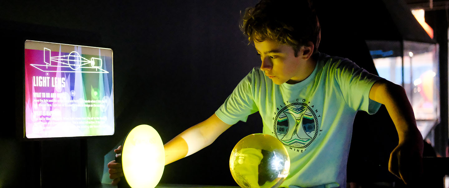 A young boy experiments with light and lenses at Science Museum Oklahoma’s hands-on optics exhibit, learning how light bends and focuses.