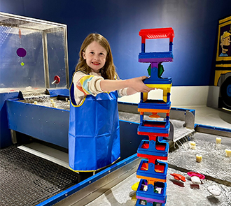 Young girl in KidsSpace at Science Museum Oklahoma building a colorful tower at an interactive water table.