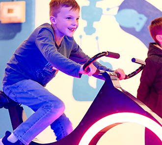 A boy pedals a glowing stationary bike in the Powerplay exhibit at Science Museum Oklahoma, learning about energy and motion through interactive science exhibits.