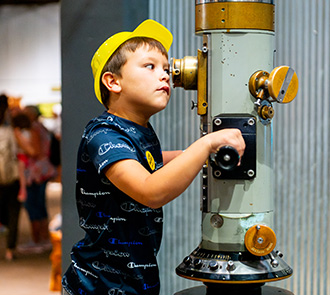 Child peers into a periscope during a STEM exhibit at Science Museum Oklahoma, discovering the science of optics through hands-on exploration.