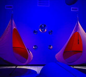 Dimly lit Sensory Space at Science Museum Oklahoma with cocoon-like hanging chairs and soothing blue lighting for sensory-friendly exploration.