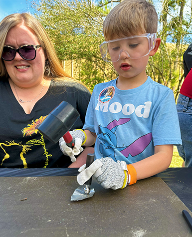A child bangs metal with a hammer outdoors at Science Museum Oklahoma.