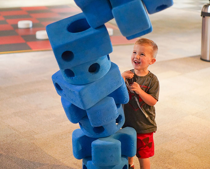 Child smiling while building with oversized foam blocks at Science Museum Oklahoma exhibit.