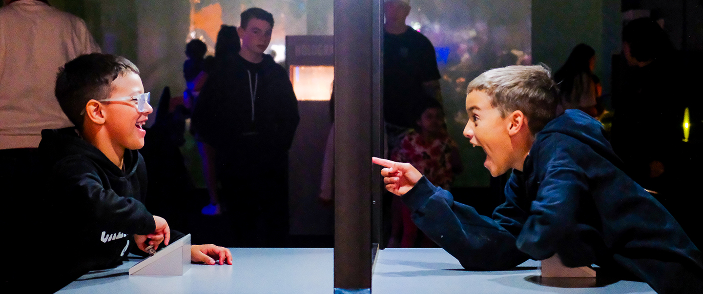 Two boys laugh and interact through a visual illusion exhibit at Science Museum Oklahoma, discovering the fun of perception and science.