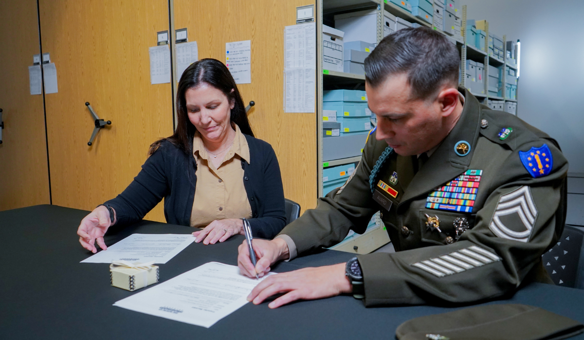 Woman, Susan Berberet, Collections Manager for Science Museum Oklahoma, and man in military uniform signing paperwork