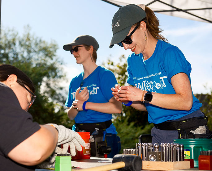 Volunteers at Science Museum Oklahoma’s DiscoverFest demonstrate hands-on STEM activities with tools, metal stamps, and outdoor science kits.
