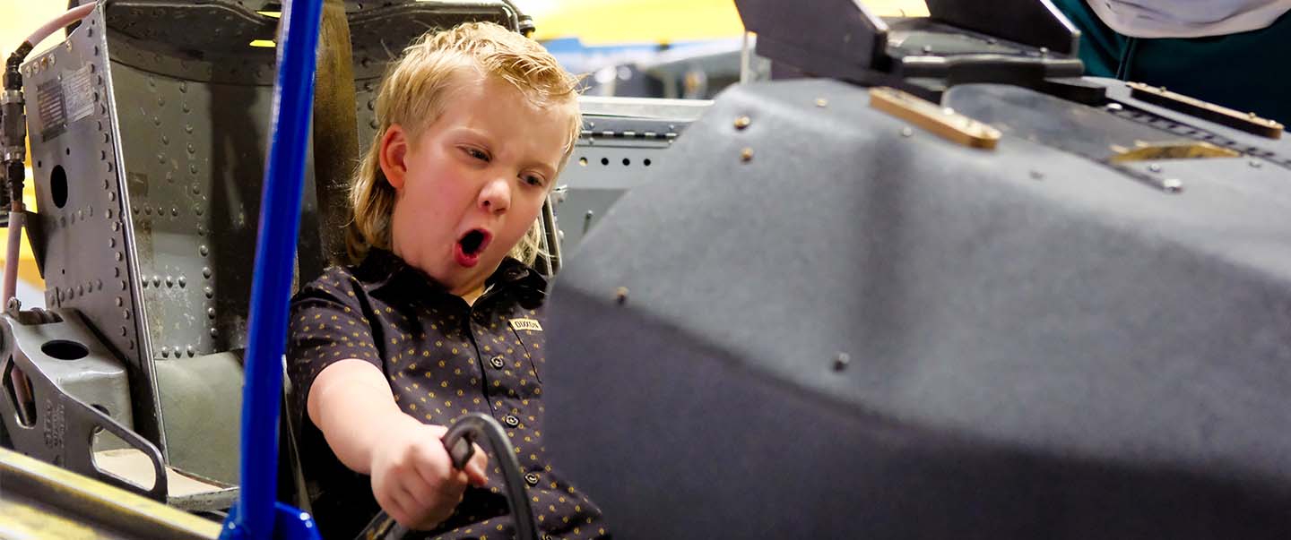 A child sits in a cockpit simulator, gripping the controls excitedly surrounded by aircraft equipment because he has a membership at Science Museum Oklahoma.