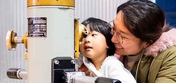 A young child explores the sky through a telescope with guidance from a parent at Science Museum Oklahoma.