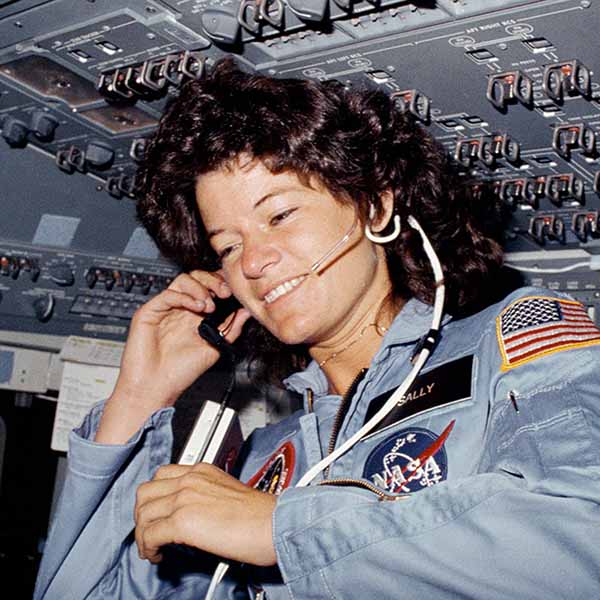 Astronaut Sally Ride inside the space shuttle cockpit wearing a NASA flight suit and headset, surrounded by control panels during her historic mission as the first American woman in space.