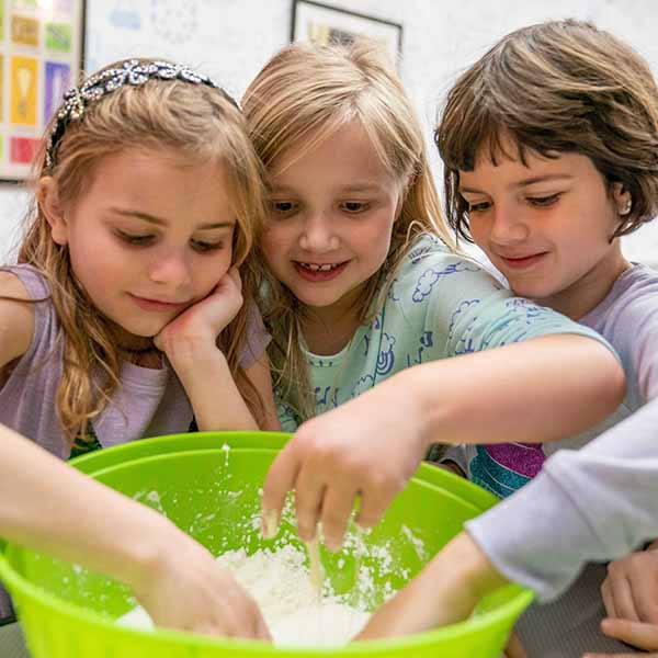 Three smiling children stick their hands in a bowl of ooblek for an experiment during a camp at Science Museum Oklahoma.