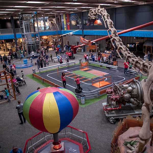 Wide view of the main exhibit floor at Science Museum Oklahoma, featuring interactive science exhibits, a large dinosaur skeleton, a colorful balloon display, and guests of all ages exploring hands-on activities.