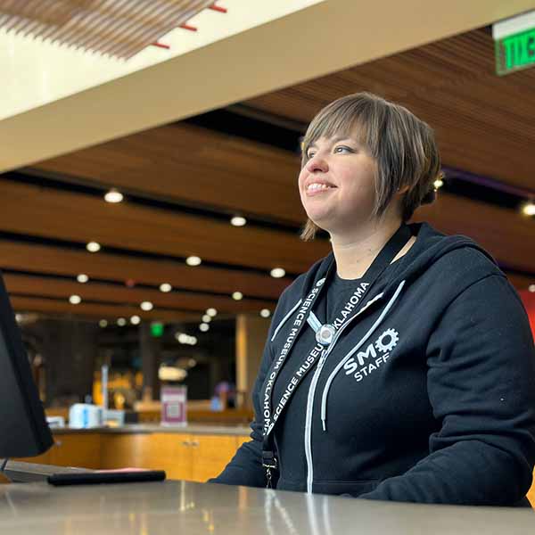 A smiling woman greets a guest at the box office of Science Museum Oklahoma.