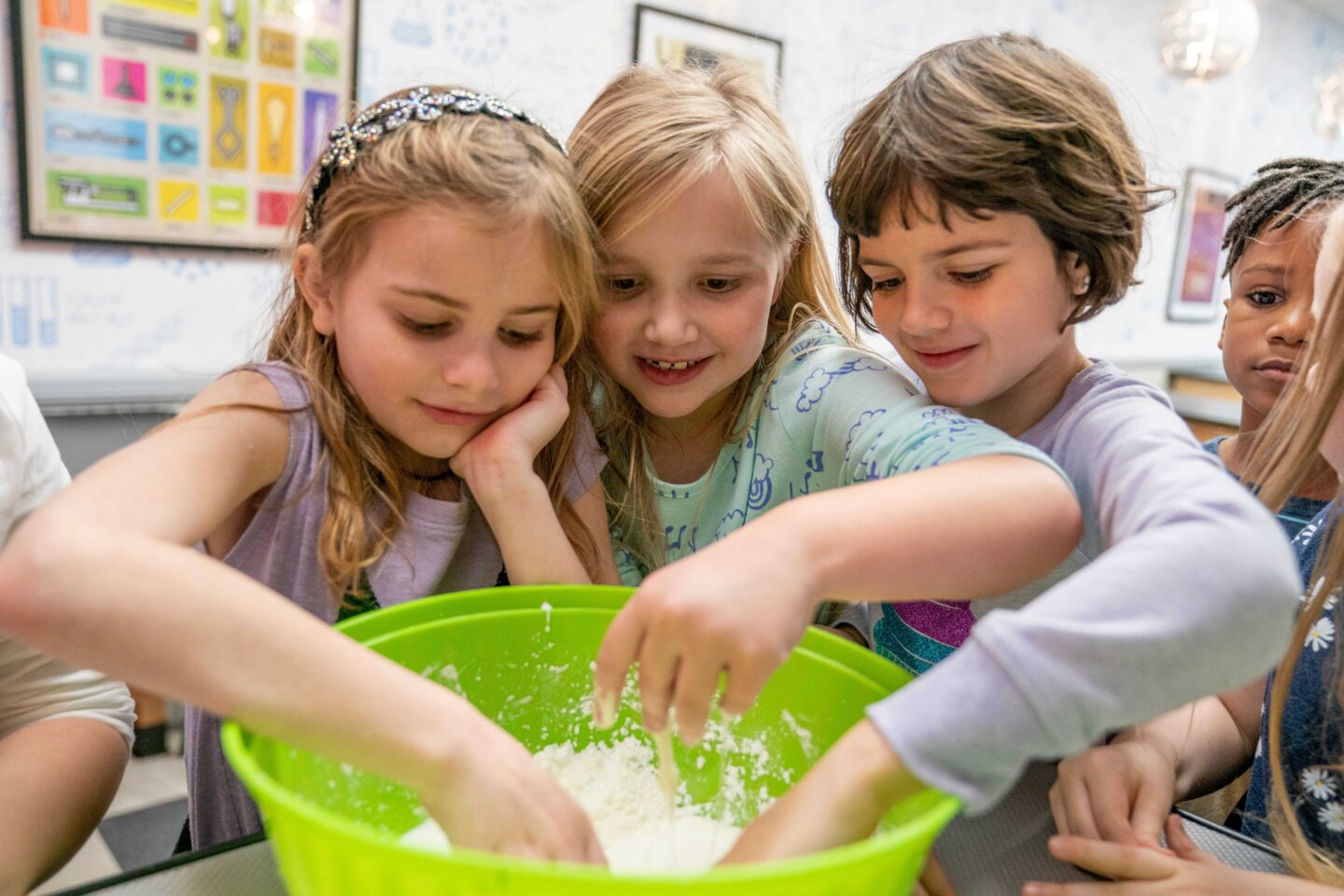 Group of young children exploring a hands-on science activity by mixing a white substance in a bright green bowl, smiling and engaged during a Science Museum Oklahoma camp or workshop.