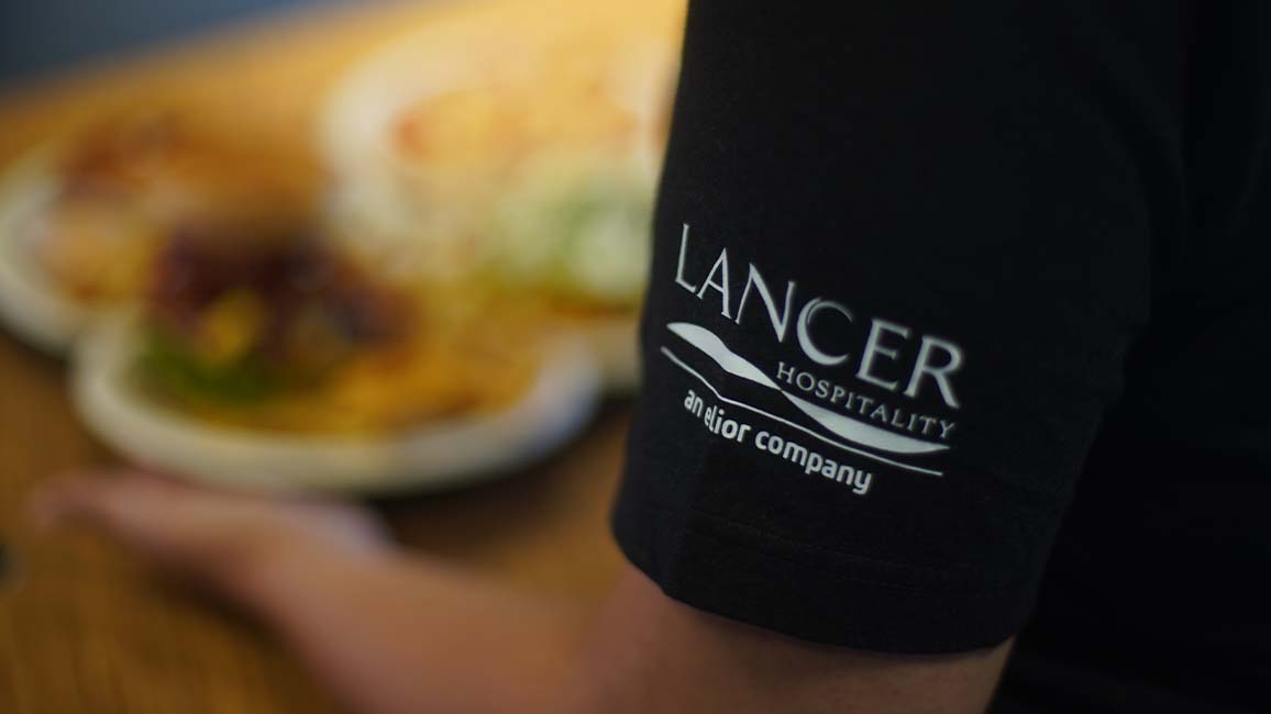 Close-up of Lancer Hospitality staff shirt with plated food in background at Science Museum Oklahoma’s Pavlov’s Café.