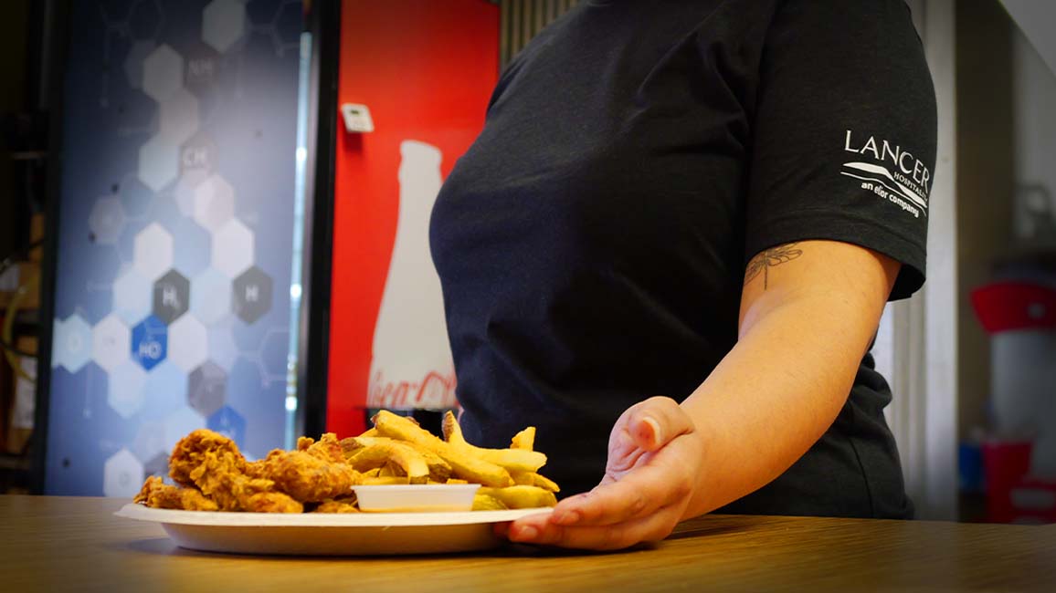A Lancer Hospitality server presents a plate of crispy chicken tenders and fries at Pavlov’s Café in Science Museum Oklahoma.