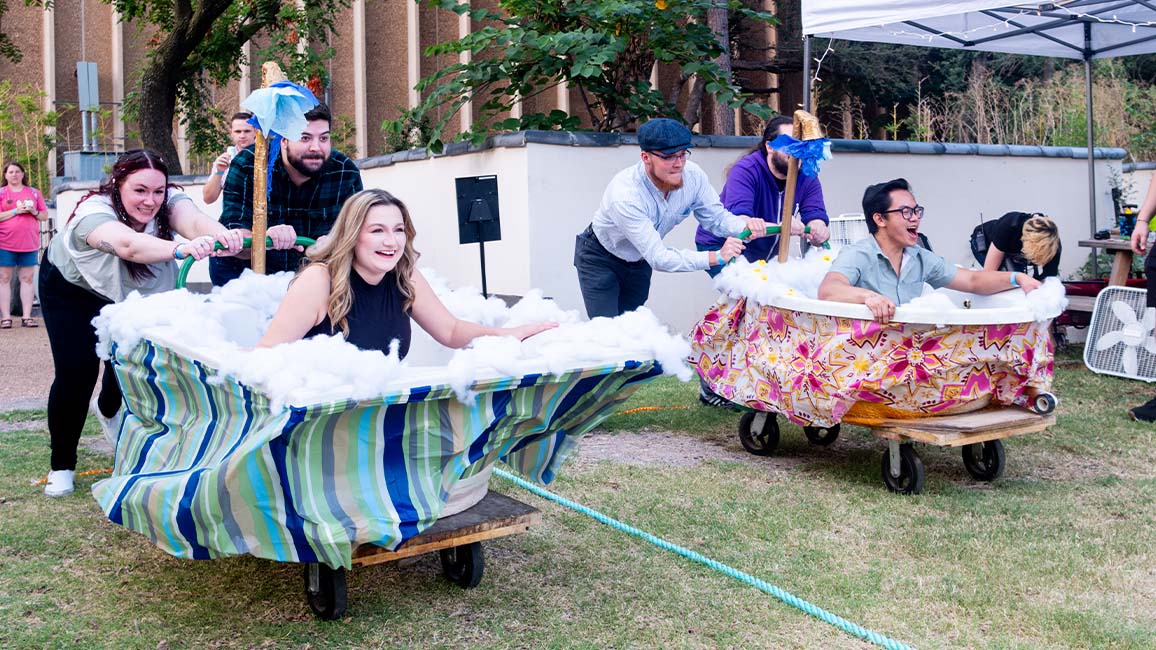 Adults race in decorated bathtubs during a quirky outdoor STEM challenge at Science Museum Oklahoma’s SMO21+ event, combining creativity, teamwork, and fun.