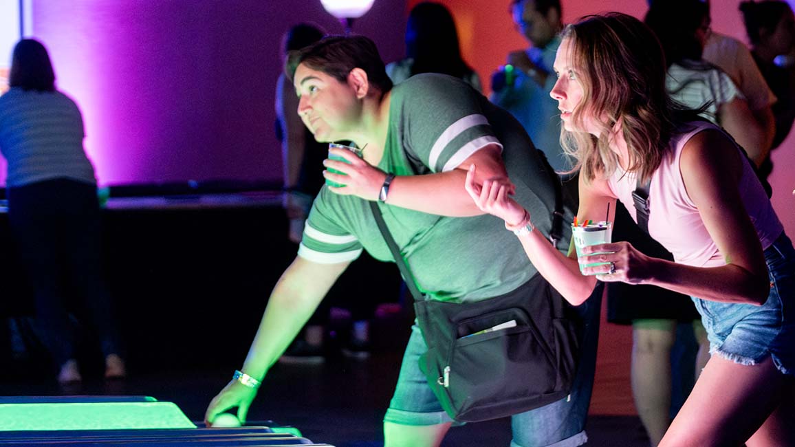 Guests play glowing arcade-style games with drinks in hand during SMO21+ at Science Museum Oklahoma, an adults-only night of science, fun, and socializing.