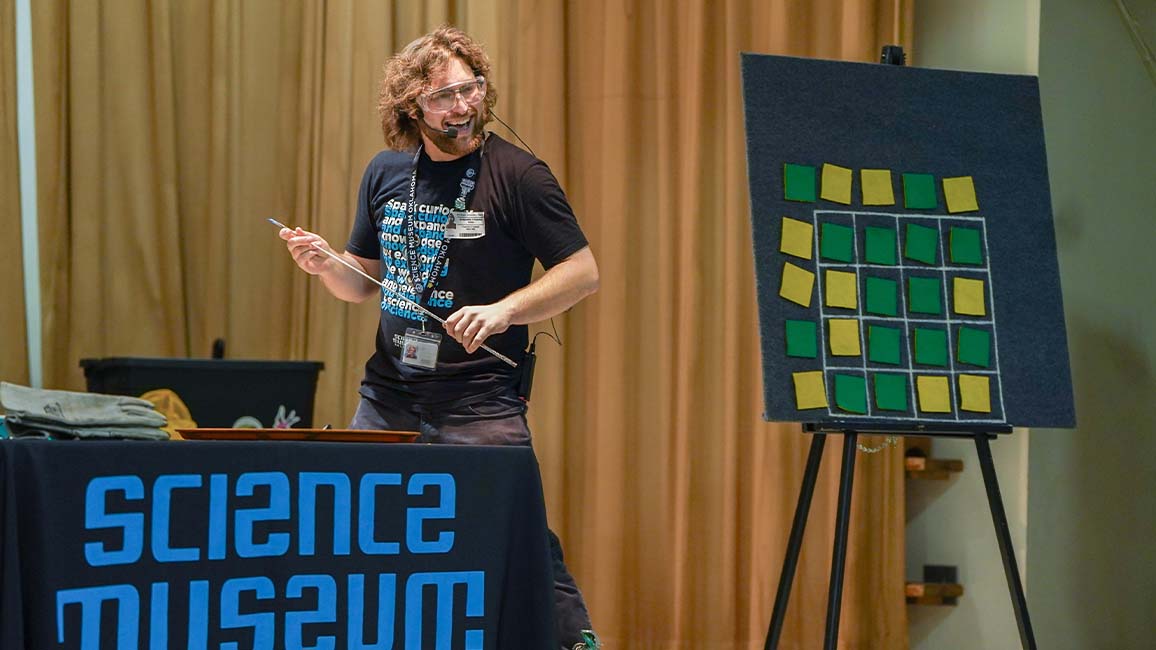 An energetic Science Museum Oklahoma presenter conducts a hands-on science activity using visual aids during a STEAM Live school program.