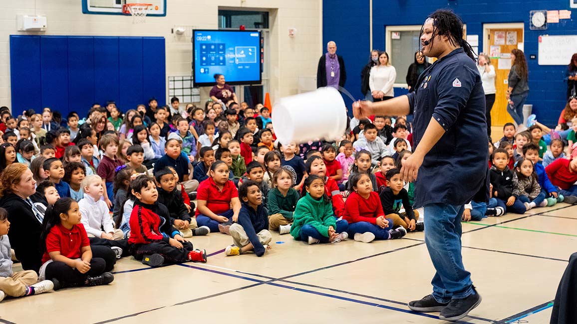 Science Museum Oklahoma educator performs a high-energy STEAM Live demonstration using a bucket cannon during a school science assembly.