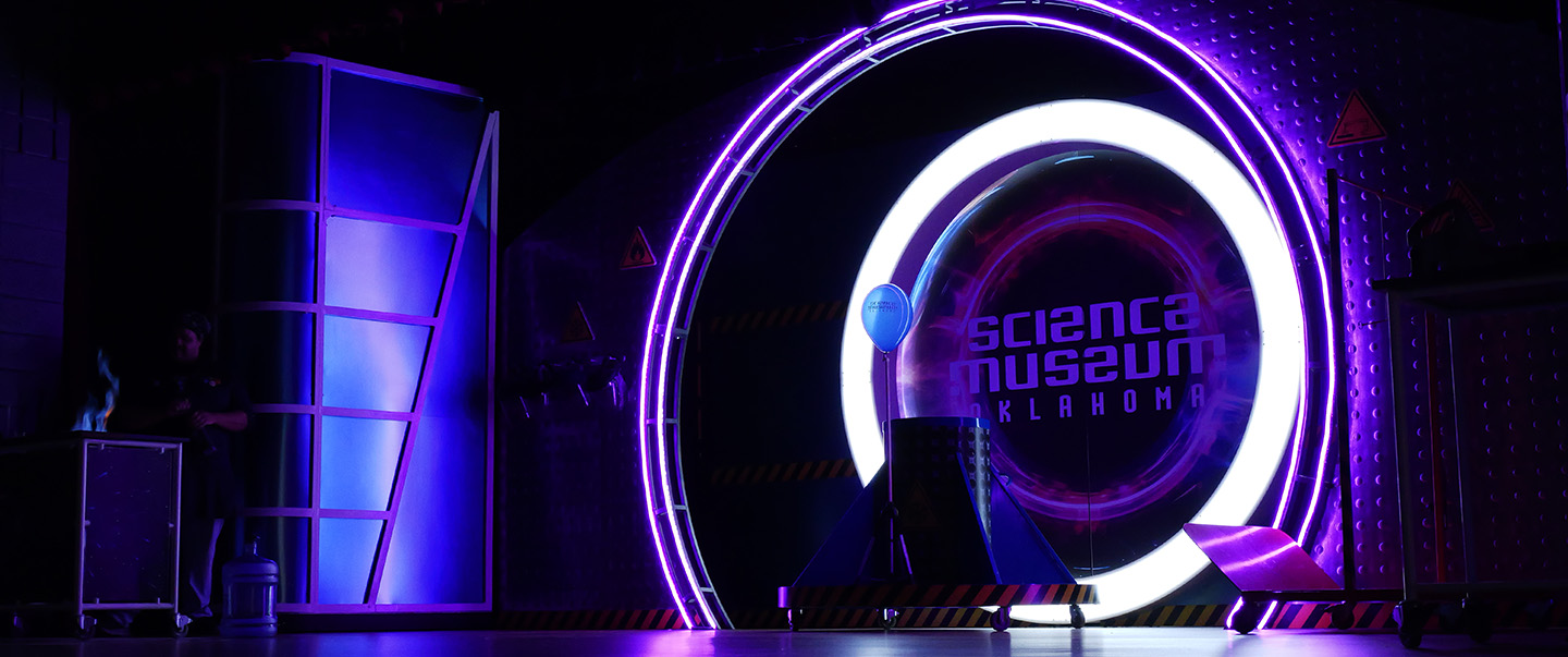 Science Live stage at Science Museum Oklahoma illuminated with dramatic purple and white lighting, featuring a glowing circular display and science equipment set up for a live demonstration.