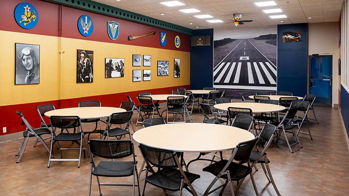 Aviation-themed party room at Science Museum Oklahoma with round tables, folding chairs, vintage photos, and a runway mural perfect for group events