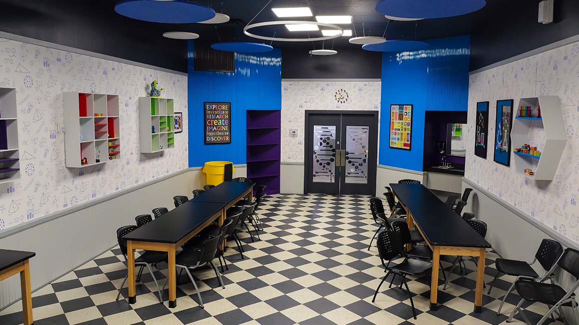 Science-inspired birthday party room at Science Museum Oklahoma featuring colorful décor, geometric shelving, checkered flooring, and long tables for kids and families.