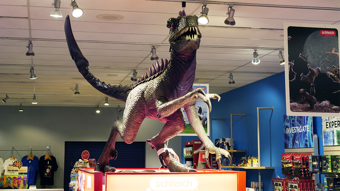 Large Schleich dinosaur figure on display inside The Science Shop at Science Museum Oklahoma, surrounded by educational toys and science-themed gifts.