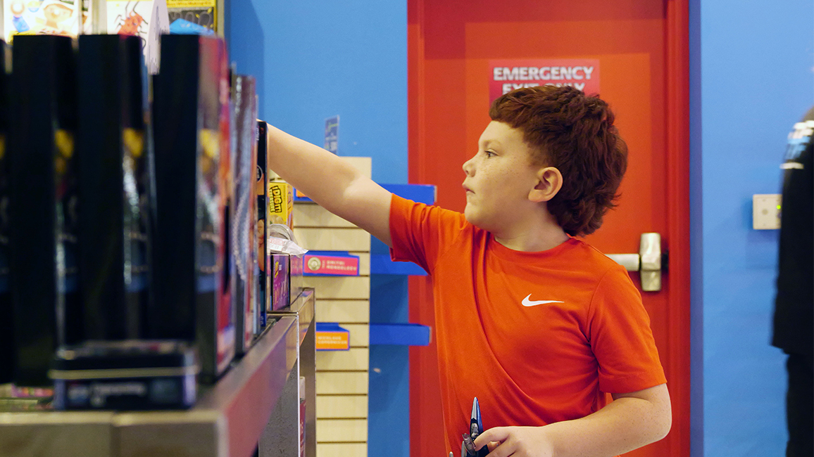 Young boy in red shirt browsing interactive science kits and educational toys in The Science Shop at Science Museum Oklahoma.