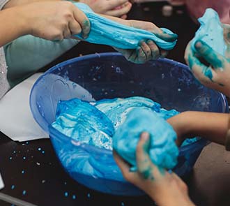 Children stretch and mold bright blue slime in a hands-on birthday party experiment at Science Museum Oklahoma.