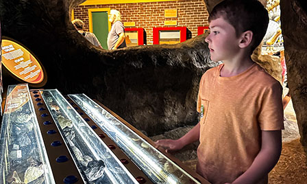 A young guest explores rocks and minerals inside a cave-themed exhibit at Science Museum Oklahoma, engaging in hands-on earth science learning.