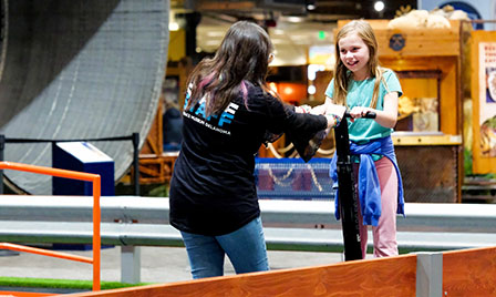 A staff member assists a child riding a segway on the segway course at Science Museum Oklahoma, part of the interactive museum experience for families.