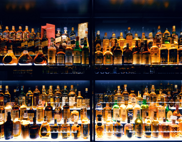 A backlit display of assorted liquor bottles arranged on glass shelves, showcasing a wide variety of spirits in different shapes, sizes, and labels.