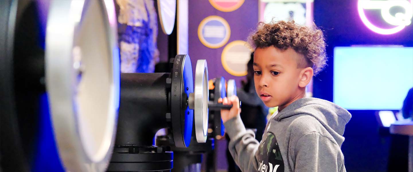 A young boy explores a hands-on physics exhibit at Science Museum Oklahoma, turning a large wheel to learn about energy and motion.