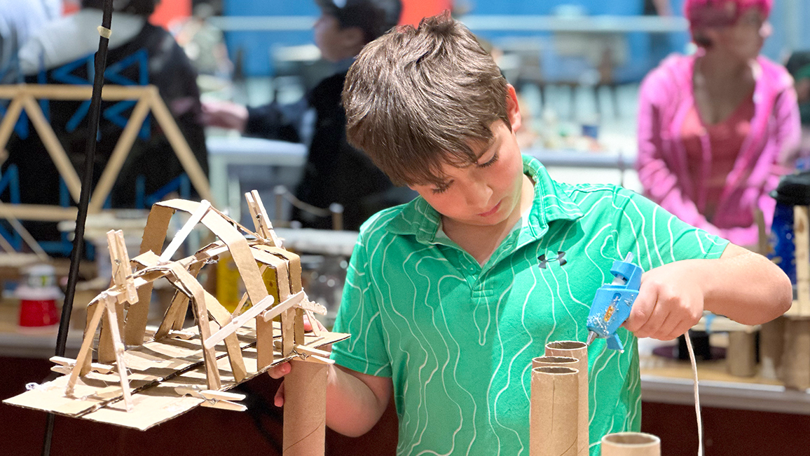 Boy with a green shirt is building a bridge out of wood in Tinkering Garag at Science Museum Oklahoma.