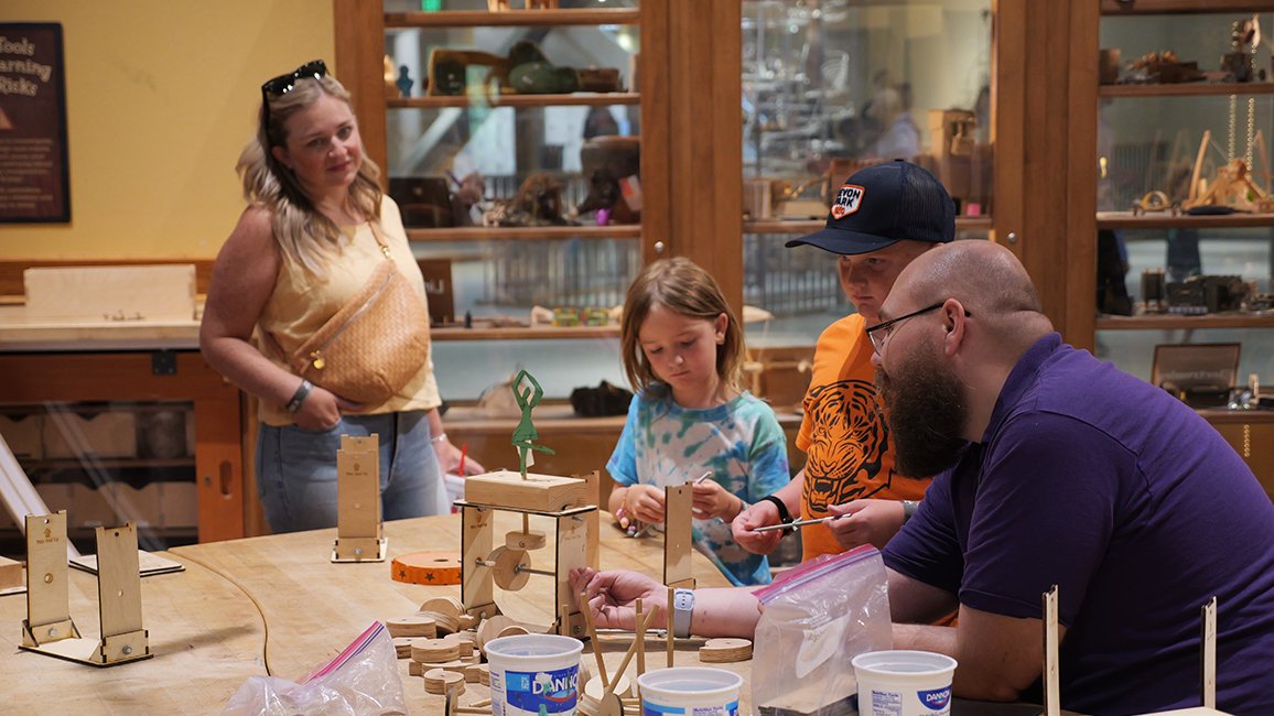 A staff member at Science Museum Oklahoma helps a family to build something in Tinkering Garage.
